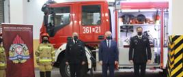 Zdjęcie przedstawia stojące w szeregu osoby uczestniczące w przekazaniu nowego samochodu ratowniczo-gaśniczego. Od lewej strażak w umundurowaniu specjalnym, Komendant Powiatowy Państwowej Straży Pożarnej w Krośnie Odrzańskim, Wojewoda Lubuski, Komendant Wojewódzki Państwowej Straży Pożarnej w Gorzowie Wlkp. Zdjęcie zrobione zostało w Garażu Jednostki Ratowniczo-Gaśniczej, na tle nowego samochodu.