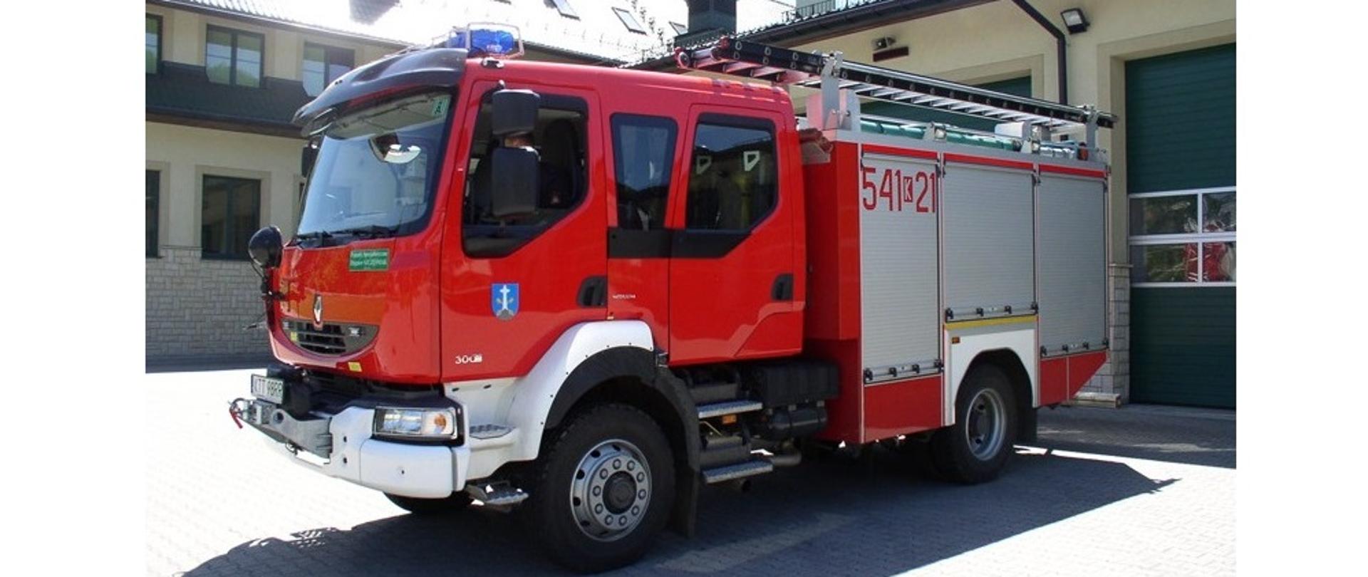 Zdjęcie przedstawia samochód pierwszowyjazdowy z zakopiańskiej Jednostki ratowniczo gaśniczej w Zakopanem. W tle Budynek Komendy Powiatowej PSP w Zakopanem. Zdjęcie zostało wykonane w słoneczny dzień.
