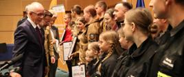 Uroczyste wręczenie nagród laureatom konkursu „Budujemy SYSTEM ODPORNOŚCI SPOŁECZNEJ” - wyróżnieni laureaci stoją na podeście sali w Podlaskim Urzędzie Wojewódzkim, organizatorzy wydarzenia wręczają dyplomy i gratulują