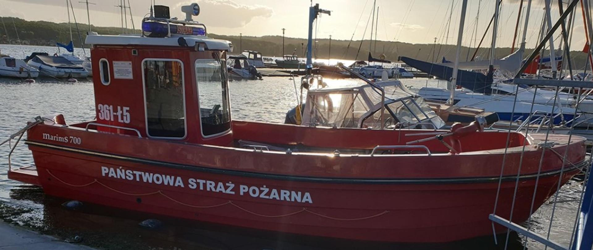 Łódź należąca do KP PSP Chojnice zacumowana przy pomoście w marnie nad jez. Charzykowskim. W tle widać inne jednostki pływające oraz część jeziora.