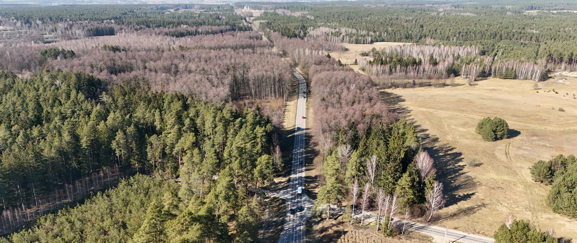 Widok na jednojezdniową drogę przecinającą las po jednej stronie i zagajnik po drugiej, widziana z lotu ptaka