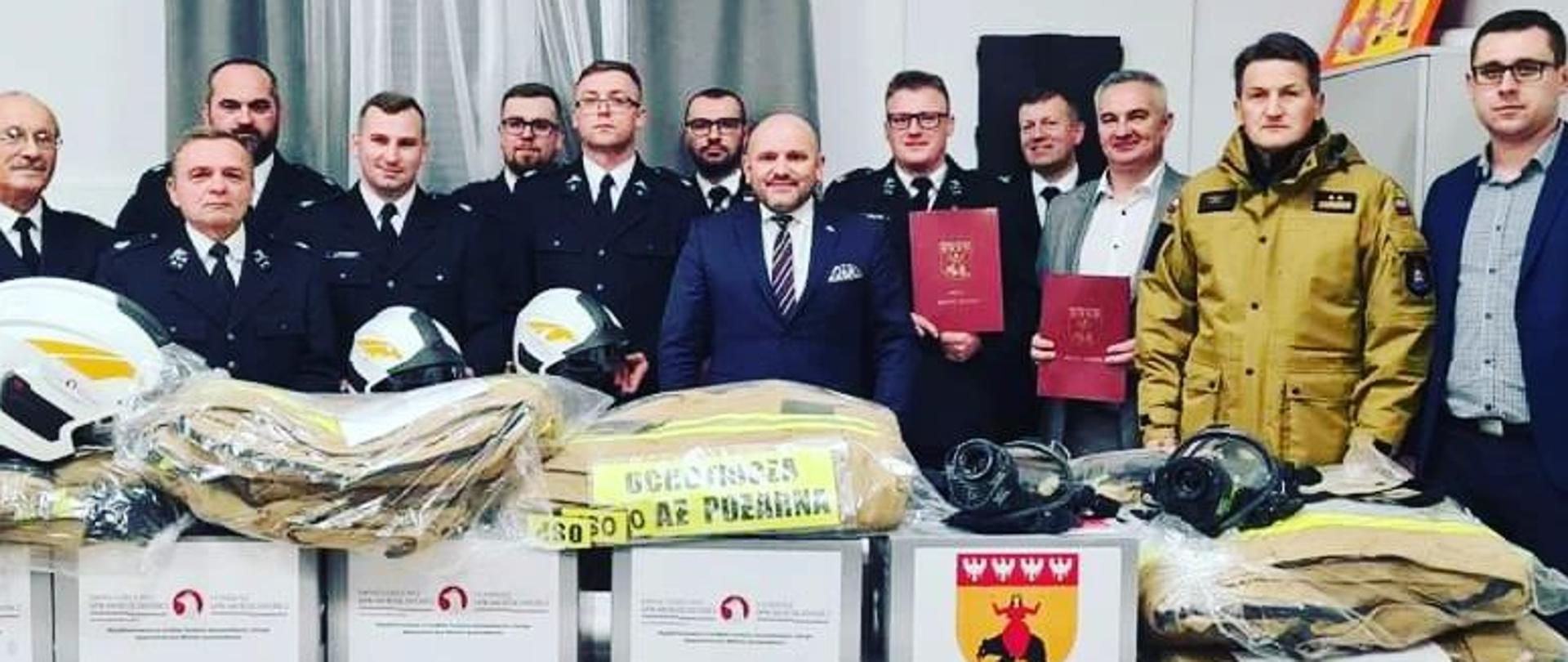 Na zdjęciu zaproszeni goście oraz druhowie. Przed nimi ułożone na stole zakupiony sprzęt pozyskany z dofinansowania.