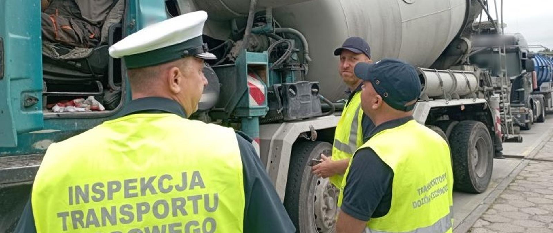 Od lewej strony: funkcjonariusz kujawsko-pomorskiej ITD i inspektorzy TDT stoją obok zatrzymanej do kontroli ciężarówki z pompą do podawania betonu. Inspektorzy rozmawiają z kierowcą pojazdu i pobierają od niego wymagane dokumenty do kontroli.