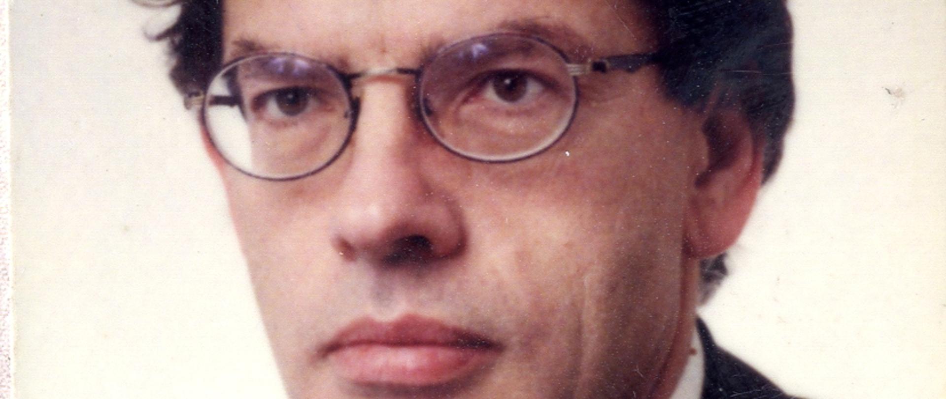 Dariusz Rosati - kolorowy portret mężczyzny, ciemne włosy, granatowa marynarka, granatowy krawat w czerwone wzory, biała koszula.