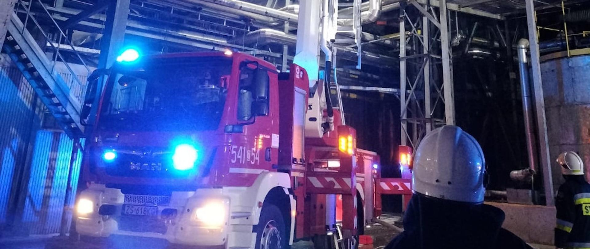 Pożar kanału technologicznego - strażacy przy pomocy podnośnika hydraulicznego podają środek gaśniczy na kanał technologiczny na wysokości.