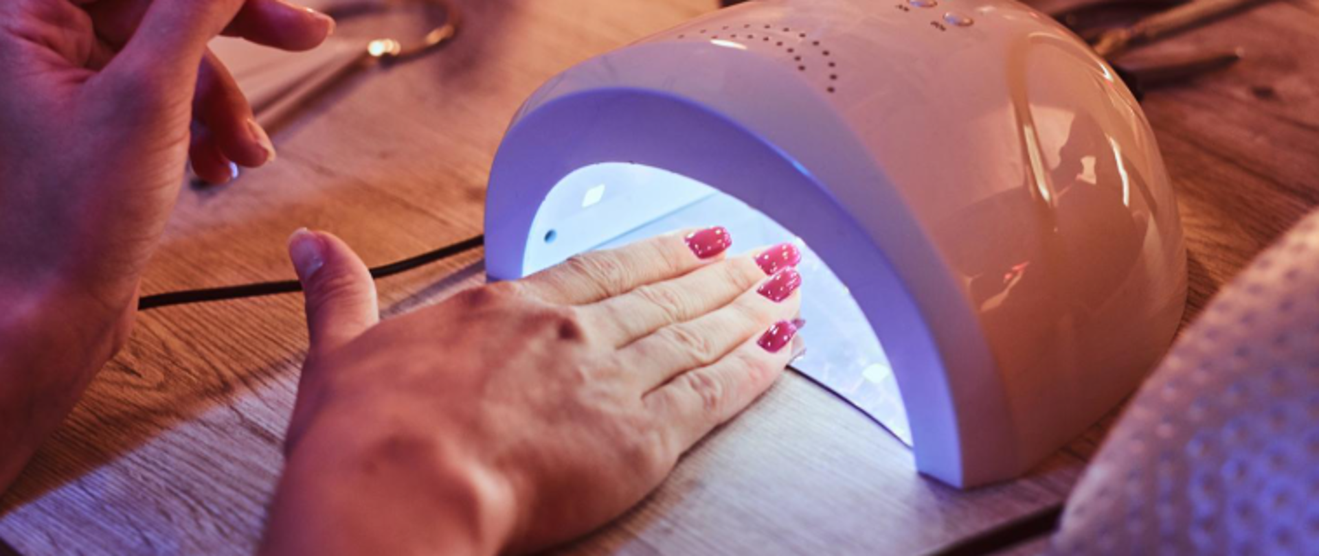 Zdjęcie przedstawia dłoń z pomaloanymi paznokciami i umiezczoną pod lampą ultrafioletową do utwardzania lakieru.