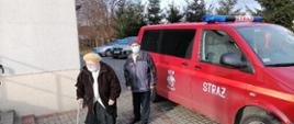 Zdjęcie przedstawia dwie starsze osoby wysiadające z samochodu OSP Nieżywięć przed punktem szczepienia przeciw COVID-19.