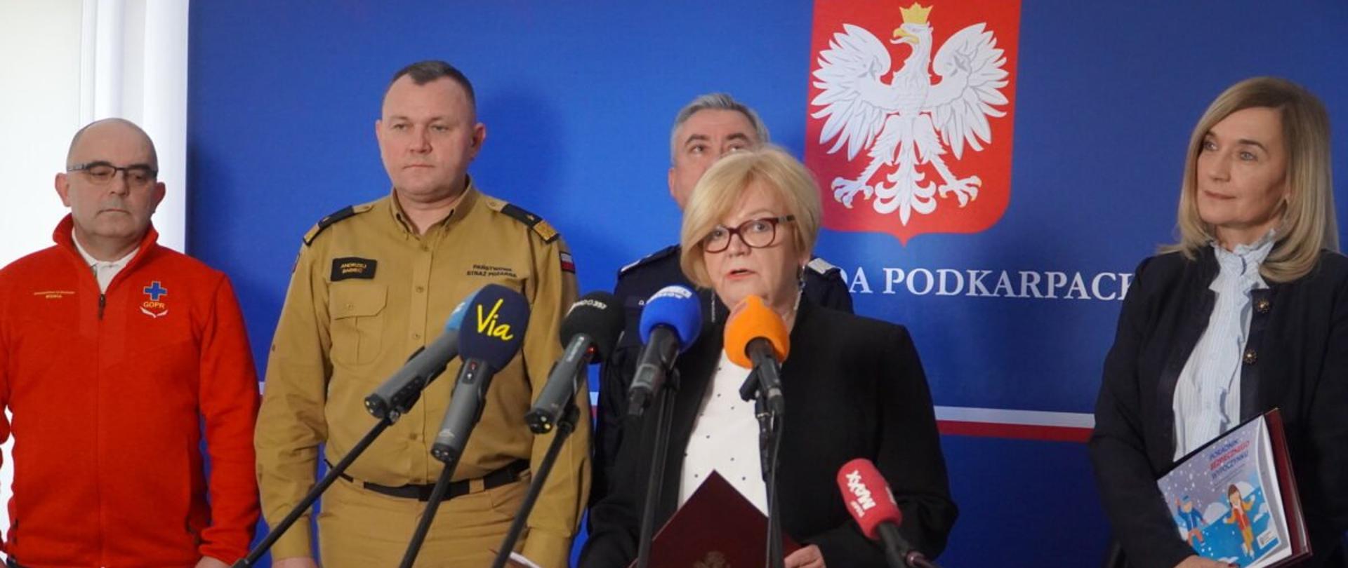Wojewoda podkarpacki Teresa Kubas-Hul zabiera głos podczas konferencji prasowej. Za wojewodą przedstawiciele Policji, Straży Pożarnej, Górskiego Ochotniczego Pogotowia Ratunkowego oraz Kuratorium Oświaty