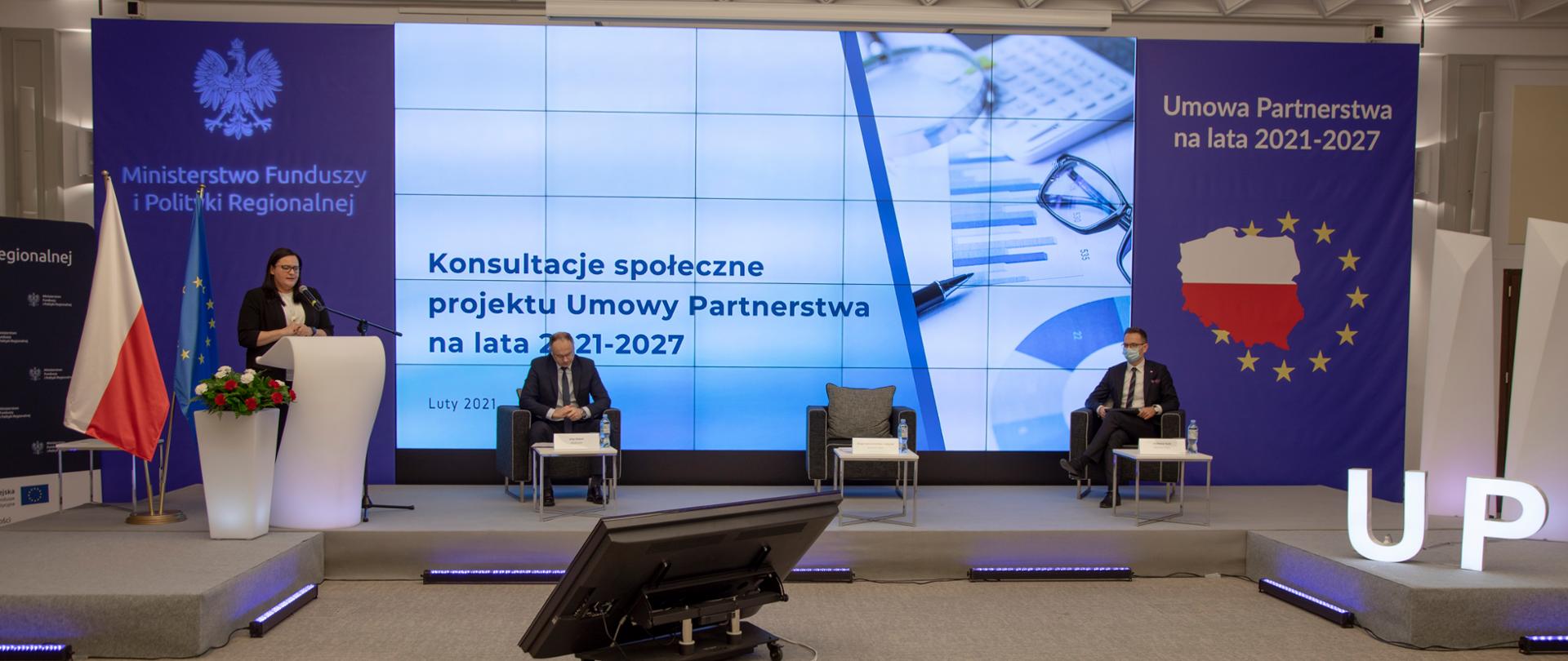 Na sali konferencyjnej od lewej - w mównicy stoi minister M. Jarosińska-Jedynak. Obok kwiaty. Za nią dwie flagi PL i UE. Na środku trzy fotele, przed każdym stolik. Z prawej strony siedzi minister Waldemar Buda.