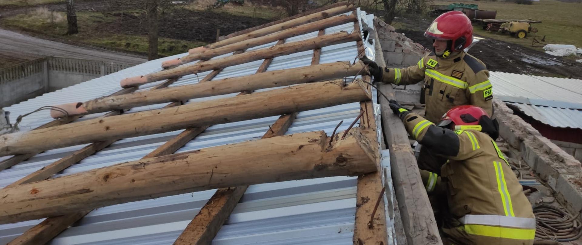 Zdjęcie przedstawia uszkodzone poszycie dachowe wykonane z blachy trapezowej oraz dwóch strażaków PSP