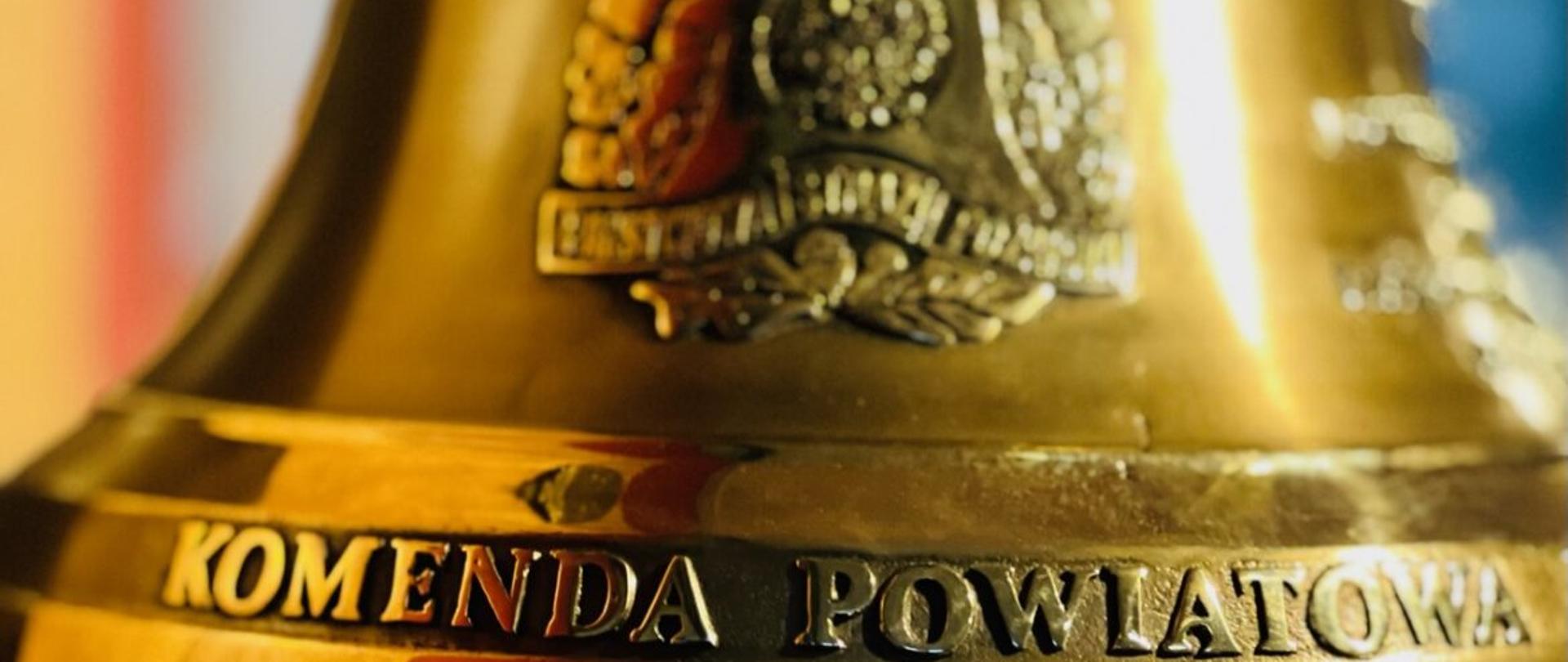 Na zdjęciu widać mosiężny dzwon, na którym widnieje logo Państwowej Straży Pożarnej oraz napis Komenda Powiatowa