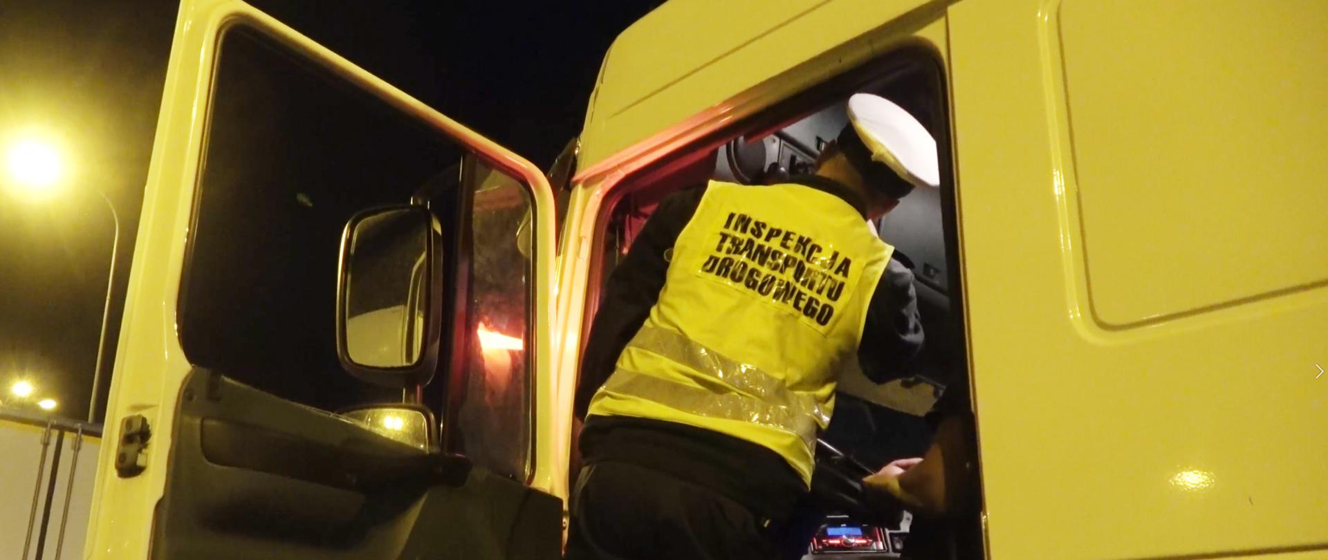 Jedna z nocnych kontroli inspektorów kujawsko-pomorskiej Inspekcji Transportu Drogowego. Na zdjęciu inspektor ITD w trakcie kontroli przy otwartych drzwiach od kabiny kierowcy. Po prawej - za kierownicą ciężarówki - kierowca.