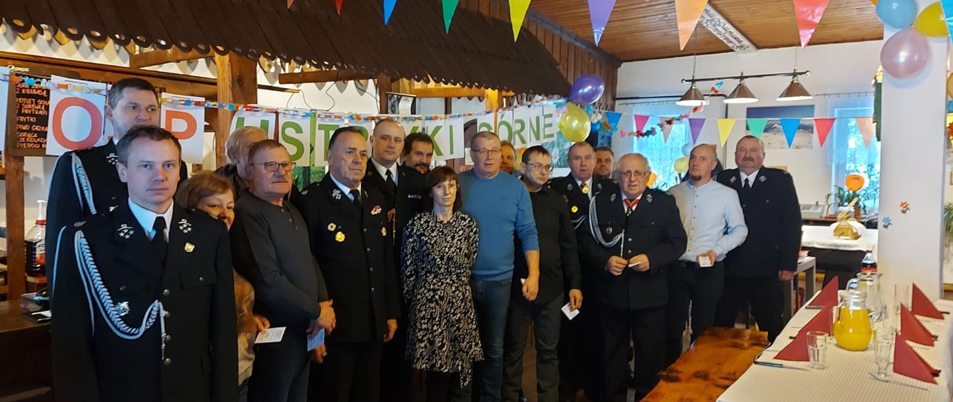 Na zdjęciu widać wszystkich zebranych na 40 leciu OSP Ustrzyki Górne. Wśród nich znajduje się komendant powiatowy PSP w Ustrzykach Dolnych mł. bryg. Emil Szmyd, Jakub Doliwa, Tadeusz Niedźwiecki oraz przedstawiciele OSP Ustrzyki Górne. Część uczestników ubranych jest w mundur galowy a reszta w ubrania cywilne.
