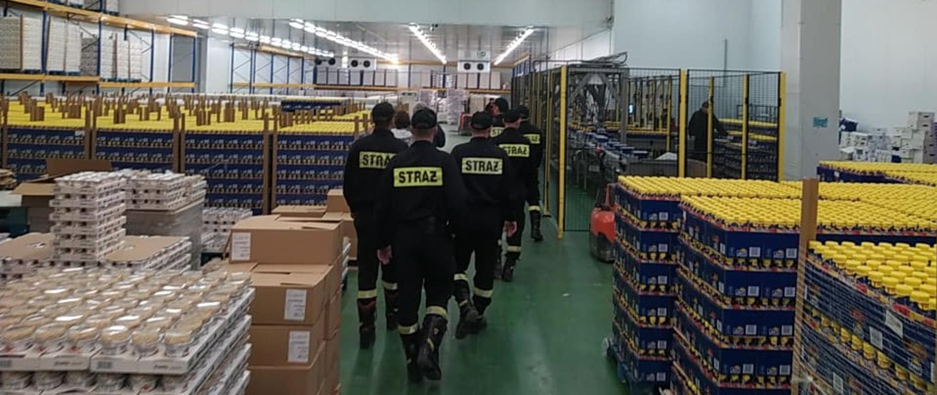 Funkcjonariusze KP PSP Kozienice na terenie hali magazynowej obiektu „Obory Sp. z o.o.” w Kozienicach, po bokach widać magazynowane produkty