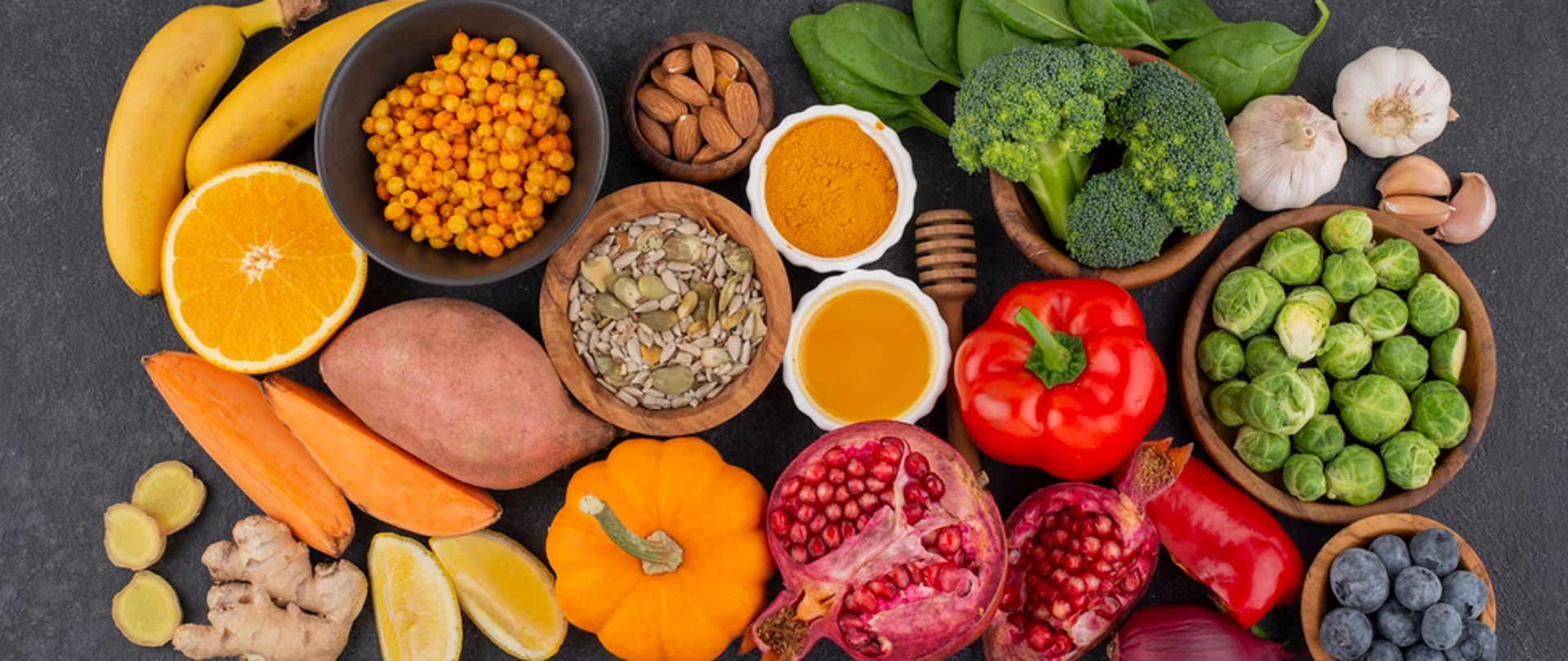 Na zdjęciu znajduje się wszelkiego rodzaju żywność (owoce, warzywa, pestki, orzechy, przyprawy). Tło jest szare.