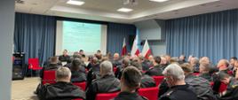 odprawa pionu kontrolno-rozpoznawczego PSP województwa mazowieckiego. uczestnicy siedzą na krzesłach w sali konferencyjnej. na przodzie przy mównicy siedzi zastępca mazowieckiego komendanta PSP oraz naczelnicy wydziału kontrolno-rozpoznawczego komendy wojewódzkiej psp w warszawie. w tle wyświetlana jest prezentacja na rzutniku.