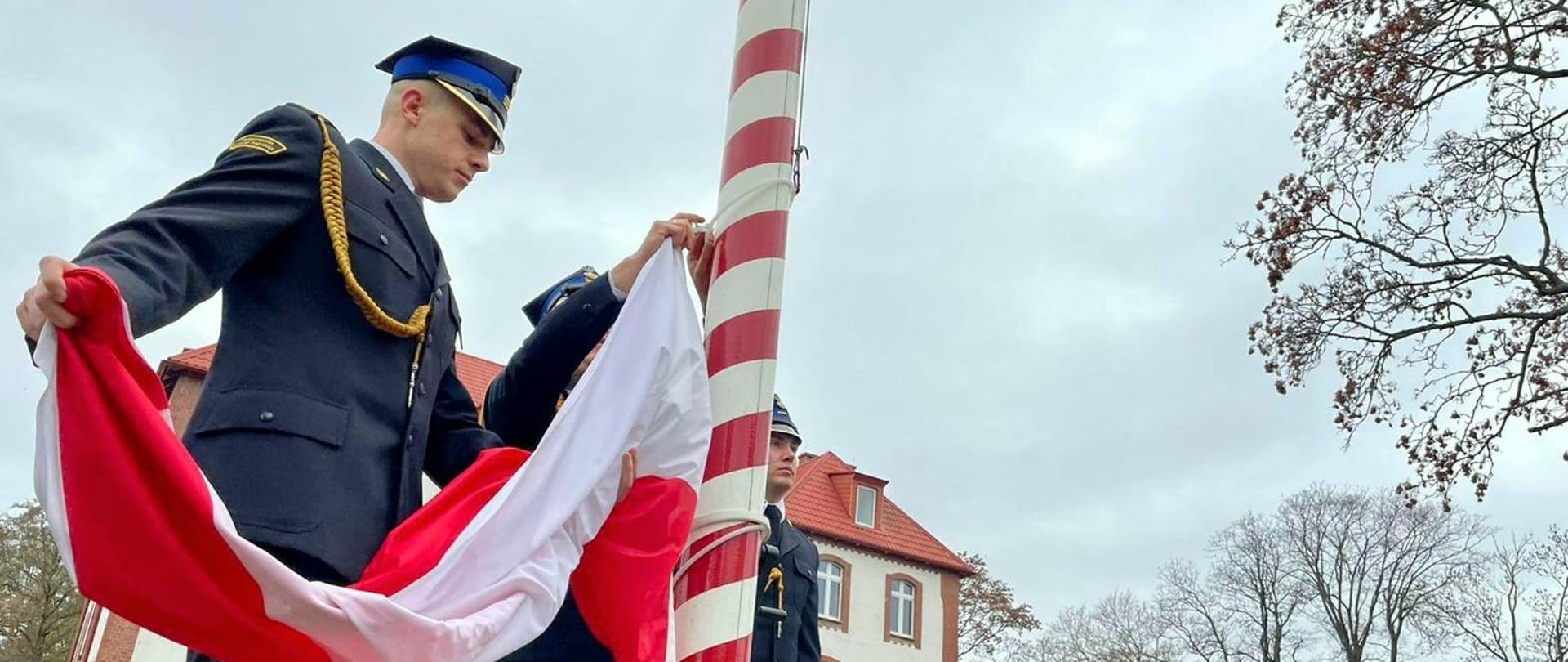 Zdjęcie przedstawia funkcjonariusza wciągającego flagę na maszt.