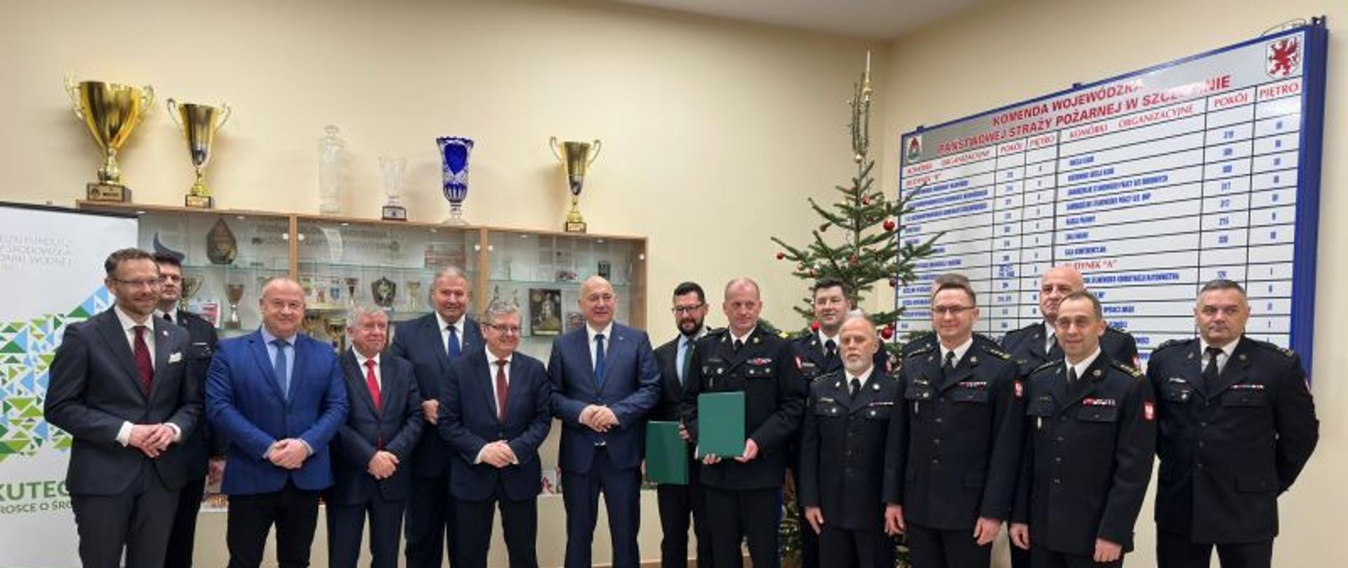 Zdjęcie grupowe, w tle puchary, choinka, roll`upy WFOŚiGW