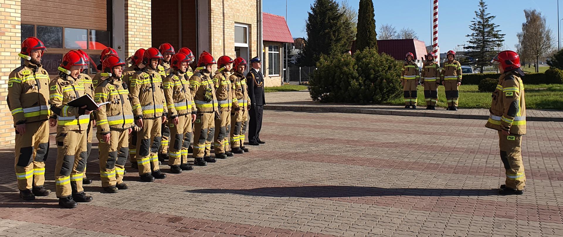 Strażacy stojący w dwóch rzędach podczas apelu na placu KP