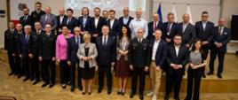 Zdjęcie grupowe uczestników Wyższego Kursu Ochrony Ludności w Akademii Pożarniczej, na tle ekranu z nazwą kursu i flag narodowych.