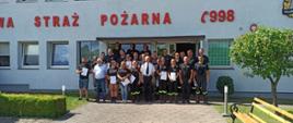 Zdjęcie przedstawia grupę ludzi przed budynkiem komendy straży pożarnej w Świdwinie. Na ścianie widzimy napis Straż Pożarna 998.