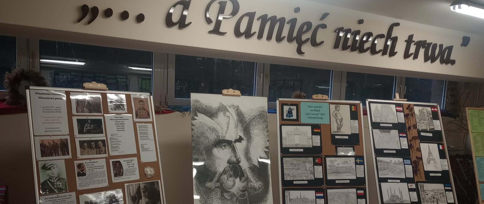 Na zdjęciu znajduje się fragment wystawy historycznej prezentowanej we wnętrzu budynku. Na ścianie widnieje napis „a Panieć miał trw…”. Przed nim ustawiono kilka plansz wystawowych z fotografiami, dokumentami, ilustracjami i opisami. Centralną część ekspozycji zajmuje duża czarno-biała ilustracja przedstawiająca portret mężczyzny. Na dole znajduje się tablica z chronologią wydarzeń. Wystawa ma charakter edukacyjny i dokumentalny.