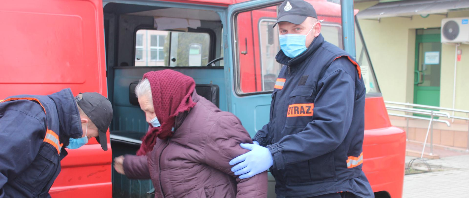 Starsza kobieta stojąca przy samochodzie jednostki OSP Dąbrówka zaparkowanym przed przychodnią