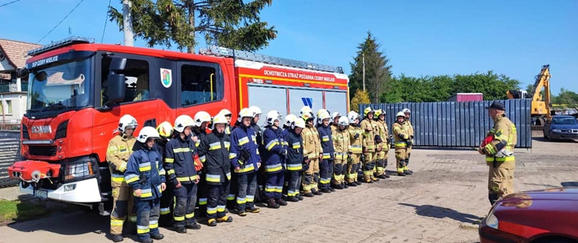 Zdjęcie przedstawia strażaków ratowników OSP na tle samochodu strażackiego, podczas zbiórki przed ćwiczeniami.