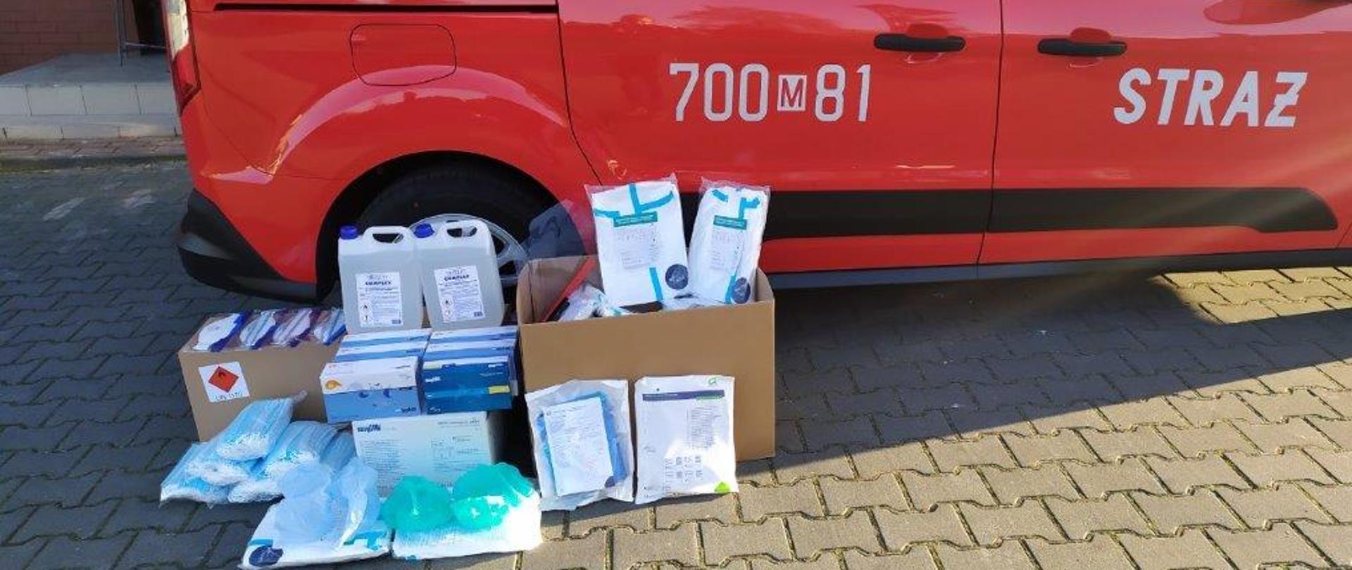 Na zdjeciu widoczne są srodki ochrony indywidualnej na tle samochodu SKw w kolorze czerwonym.