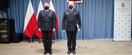 Na zdjęciu widać dwóch strażaków, w tle trzy flagi Polski oraz godło RP.