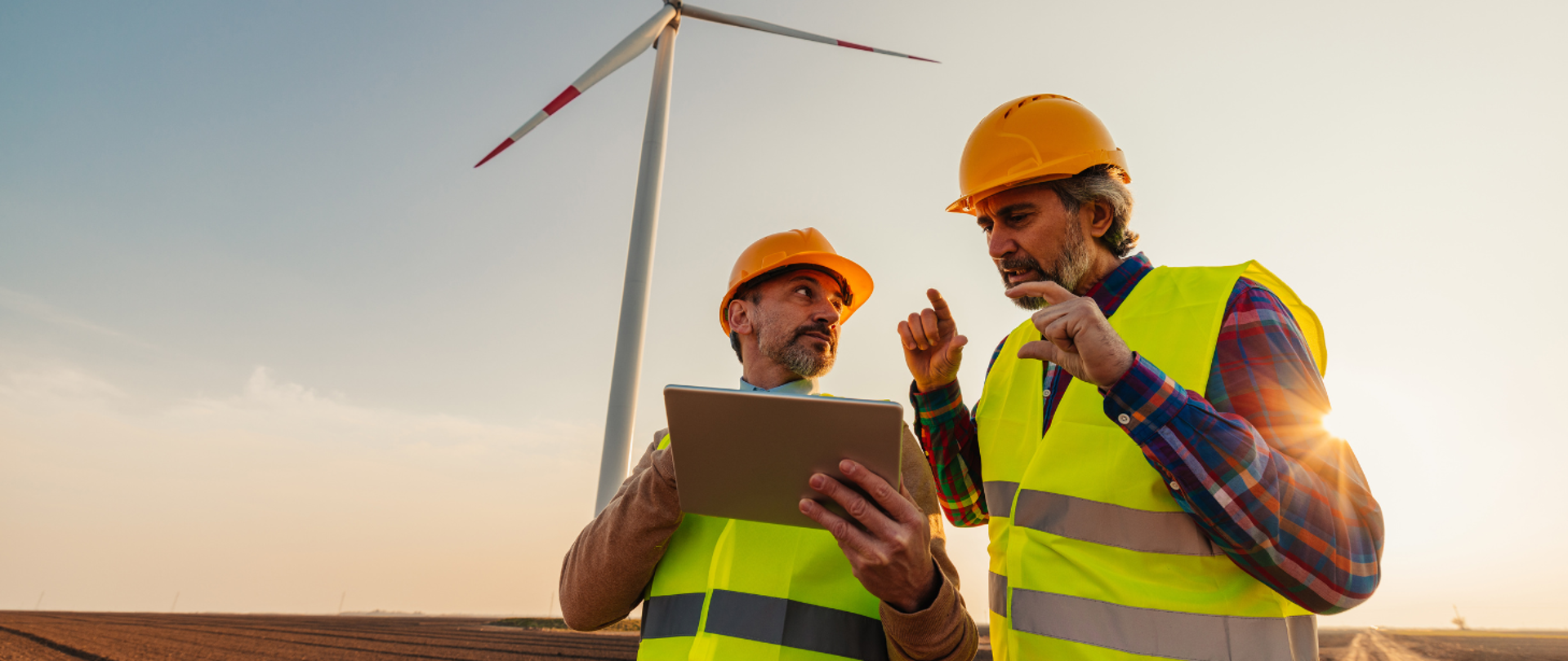 na zdjęciu widoczni są dwaj mężczyźni omawiający szczegóły projektu, za nimi na drugim planie znajduje się wiatrak. 