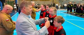 
Podczas II Halowych Młodzieżowych Zawodów Sportowo-Pożarniczych na hali sportowej wręczane są medale młodym uczestnikom ubranym w stroje drużynowe.
