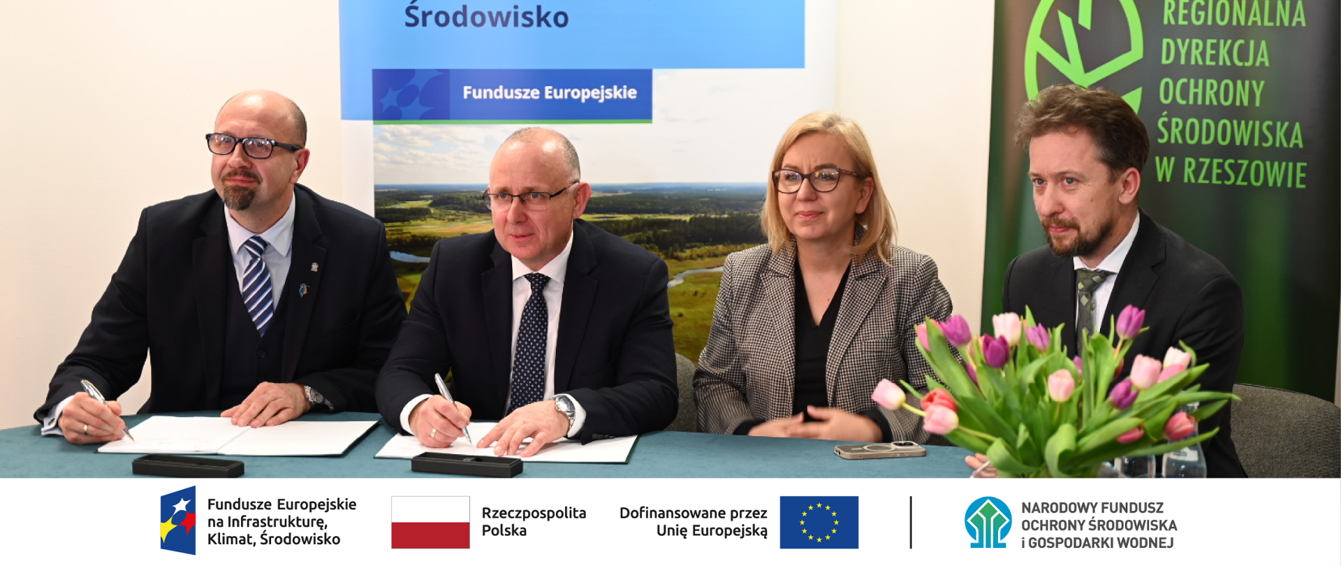 Zdjęcie grupowe. W stopce grafiki ciąg logotypów: Fundusze Europejskie na Infrastrukturę, Klimat, Środowisko, flaga Rzeczypospolita Polska, flaga UE i Dofinansowane przez UE, NFOŚiGW.