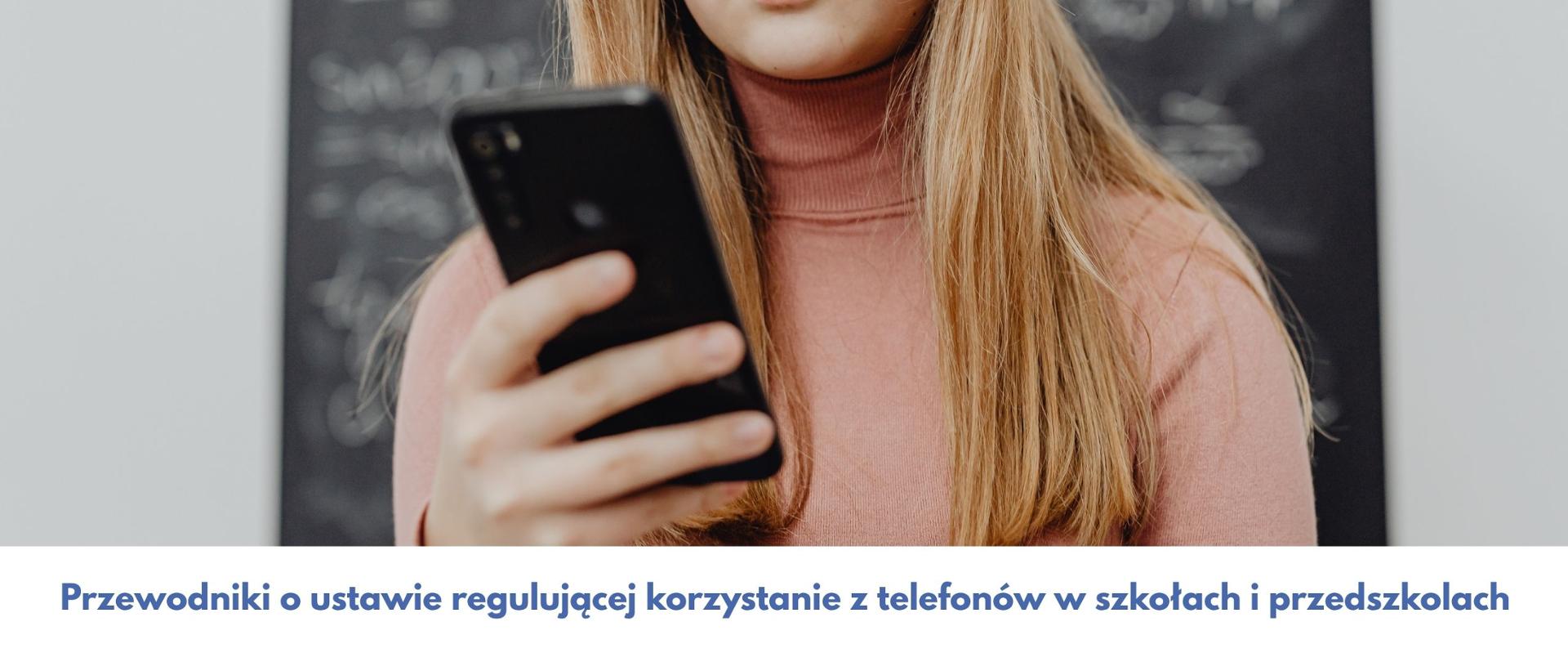 Telefon komórkowy w dłoni dziewczynki, a poniżej niebieski napis na białym tle: przewodniki o ustawie regulującej korzystanie z telefonów w szkołach i przedszkolach