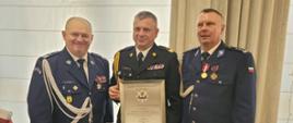 Pomorski komendant wojewódzki Państwowej Straży Pożarnej stoi trzymając wyróżnienie obok stoi kierownictwo Komendy Wojewódzkiej Policji.