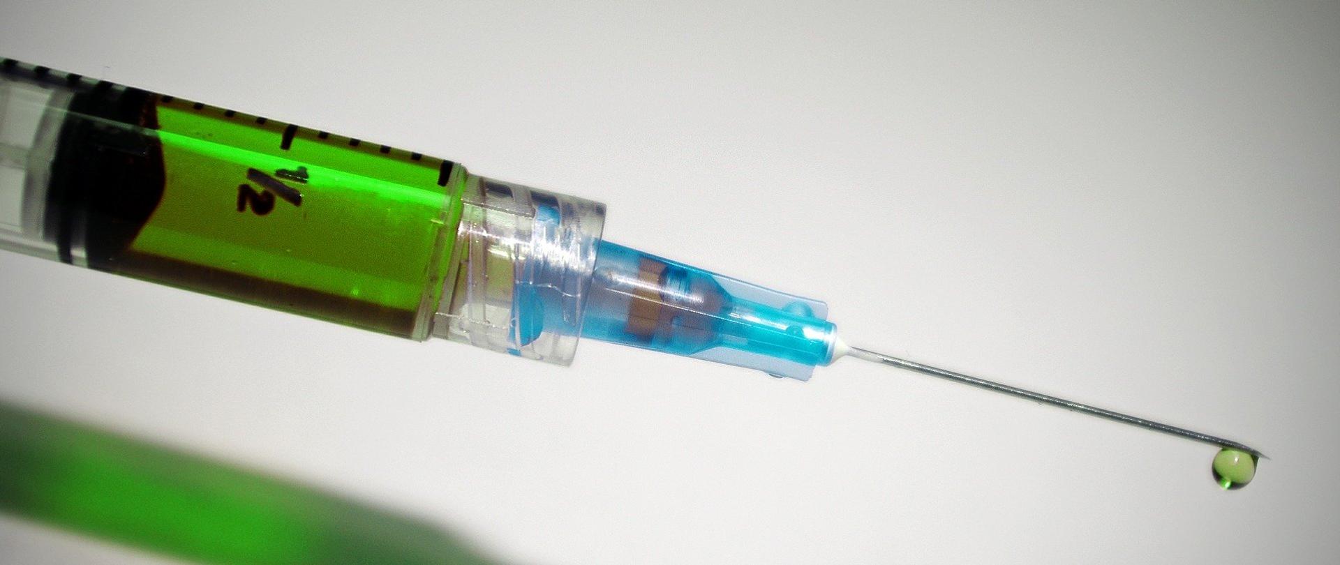 strzykawka z zielonym płynem na białym blacie.