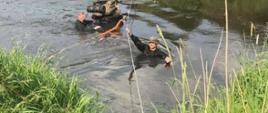 Osoby przechodzą przez rzekę. Sześć osób asekuruje się za pomocą liny.