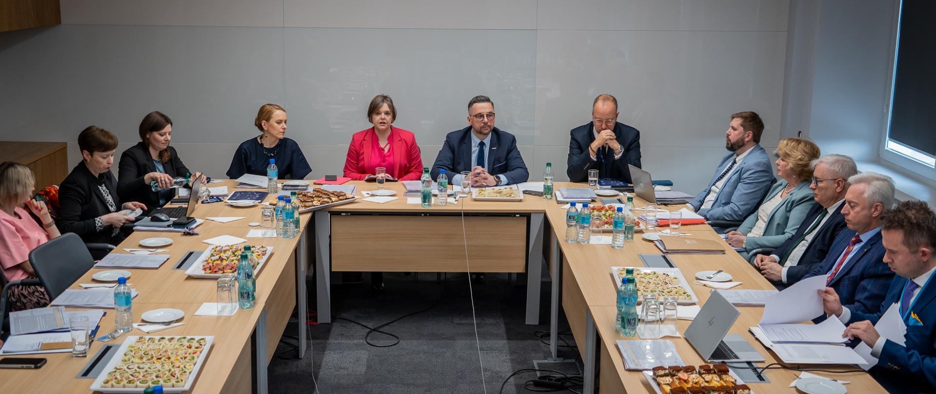 Widok od tyłu sali, za ustawionymi w czworokąt stołami siedzą ludzie, u szczytu stołu minister Kulasek i wiceminister Zioło-Pużuk.