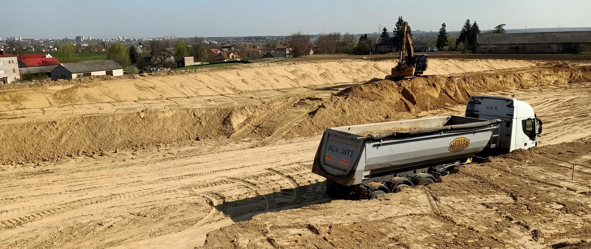 DK9 obwodnica Ostrowca Świętokrzyskiego - roboty ziemne, wykonywanie nasypu, pracująca ładowarka i samochód ciężarowy z częściowo załadowaną skrzynią 