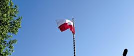 Na tle bezchmurnego nieba faluje biało-czerwona flaga na maszcie.