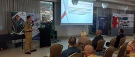 Zdjęcie przedstawia strażaków oraz osoby cywilne podczas seminarium. Osoby siedzą na krzesełkach na sali , natomiast prelegent omawia temat.