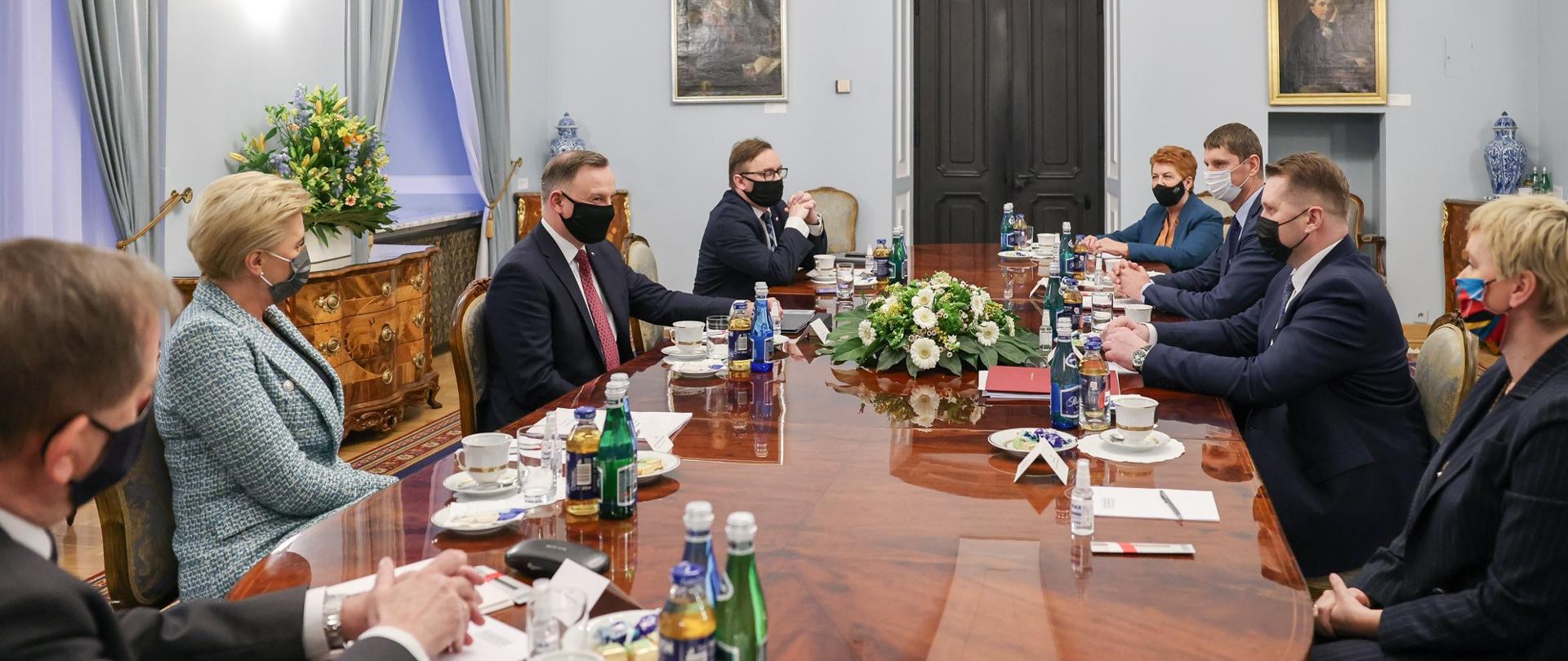 Elegancko ubrani uczestnicy spotkania Ministra Edukacji i Nauki z Prezydentem Rzeczpospolitej Polskiej siedzą przy drewnianym stole.