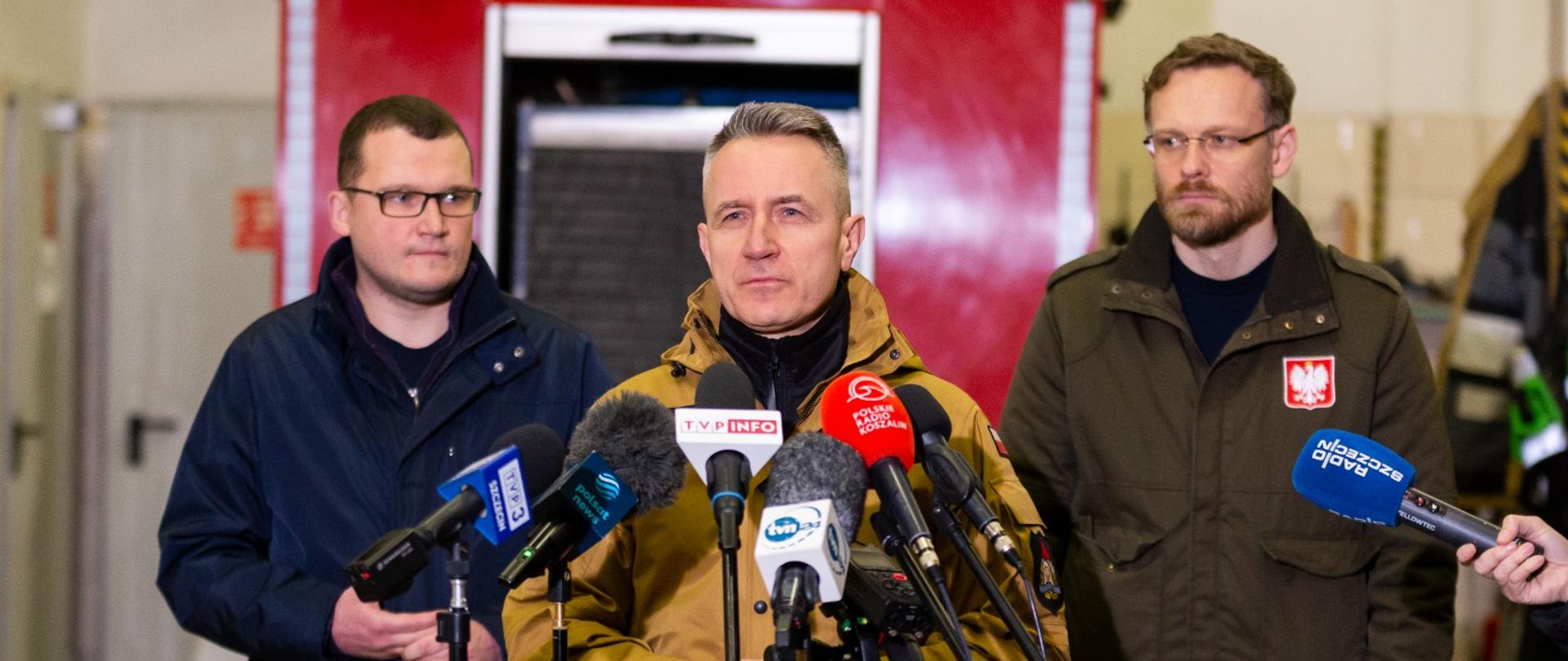 Podczas konferencji prasowej, komendant główny PSP stoi przy mikrofonie , za nim po lewo wiceminister spraw wewnętrznych, po prawo wojewoda zachodniopomorski 