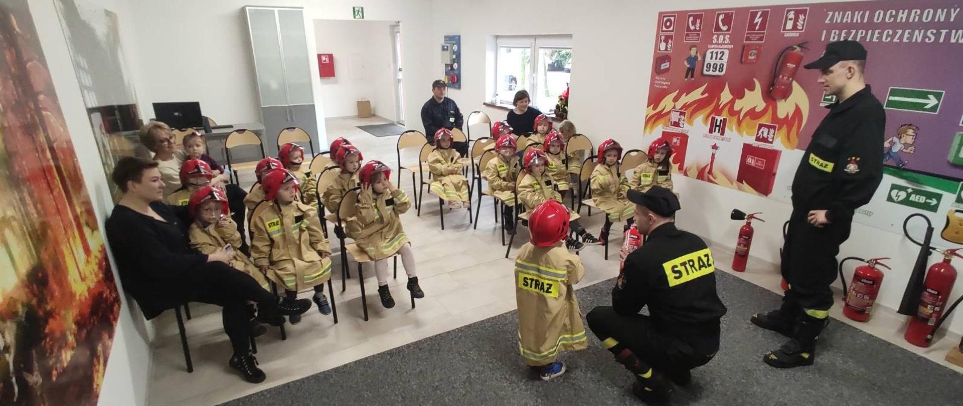 Dzieci w strojach strażackich w czasie zajęć w sali edukacyjnej. 