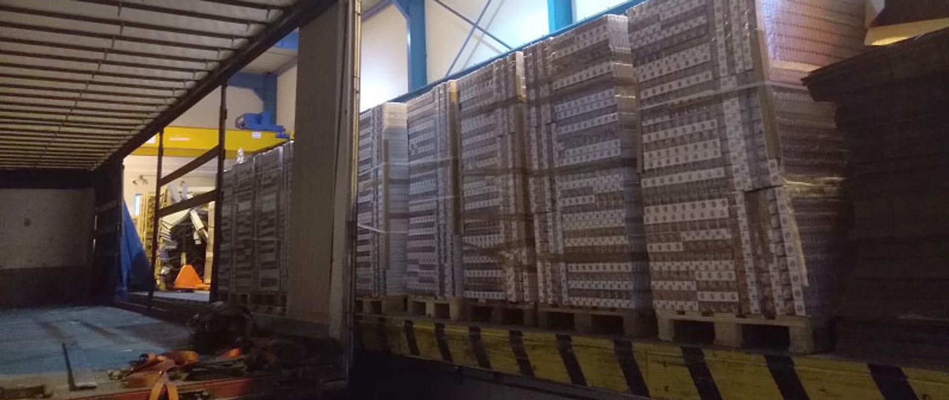 Wnętrze hali, otwarta naczepa oraz ułożone papierosy na rampie.