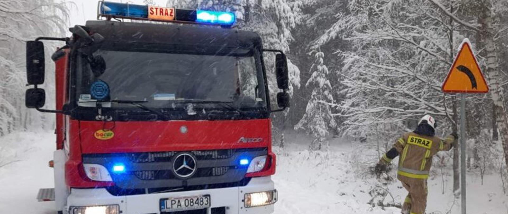 Na zdjęciu samochód ratowniczo-gaśniczy i strażak na tle zaśnieżonego krajobrazu.