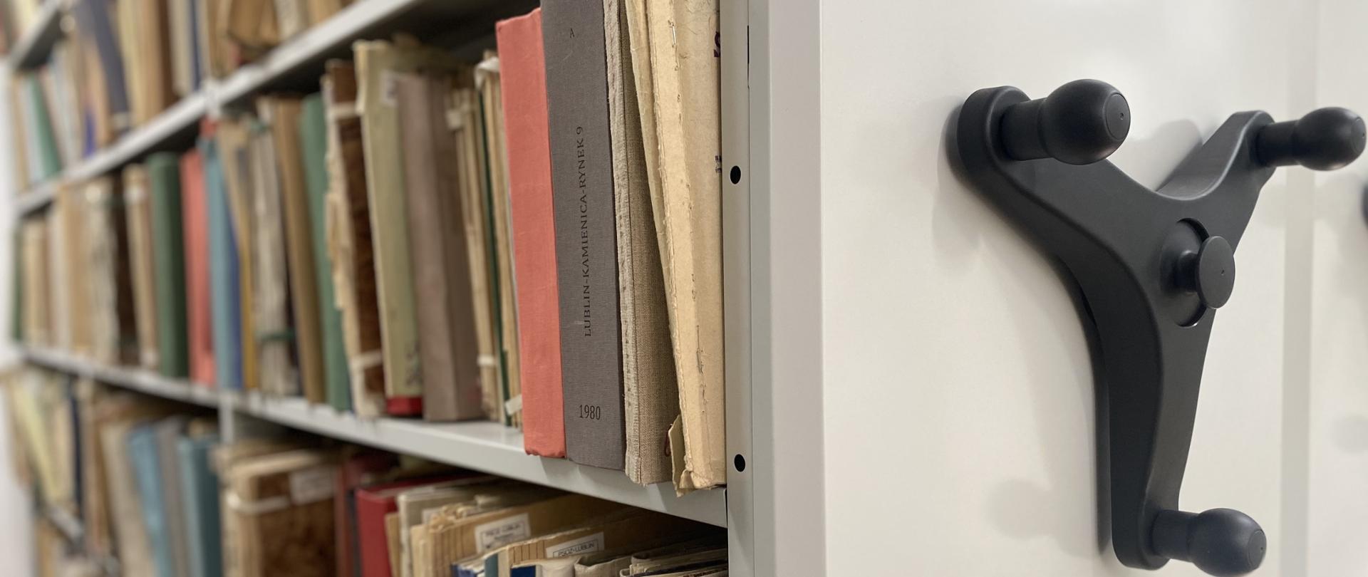 Zdjęcie przedstawia regał przesuwny z pomieszczenia archiwum, na półkach którego przechowywane są dokumentacje.