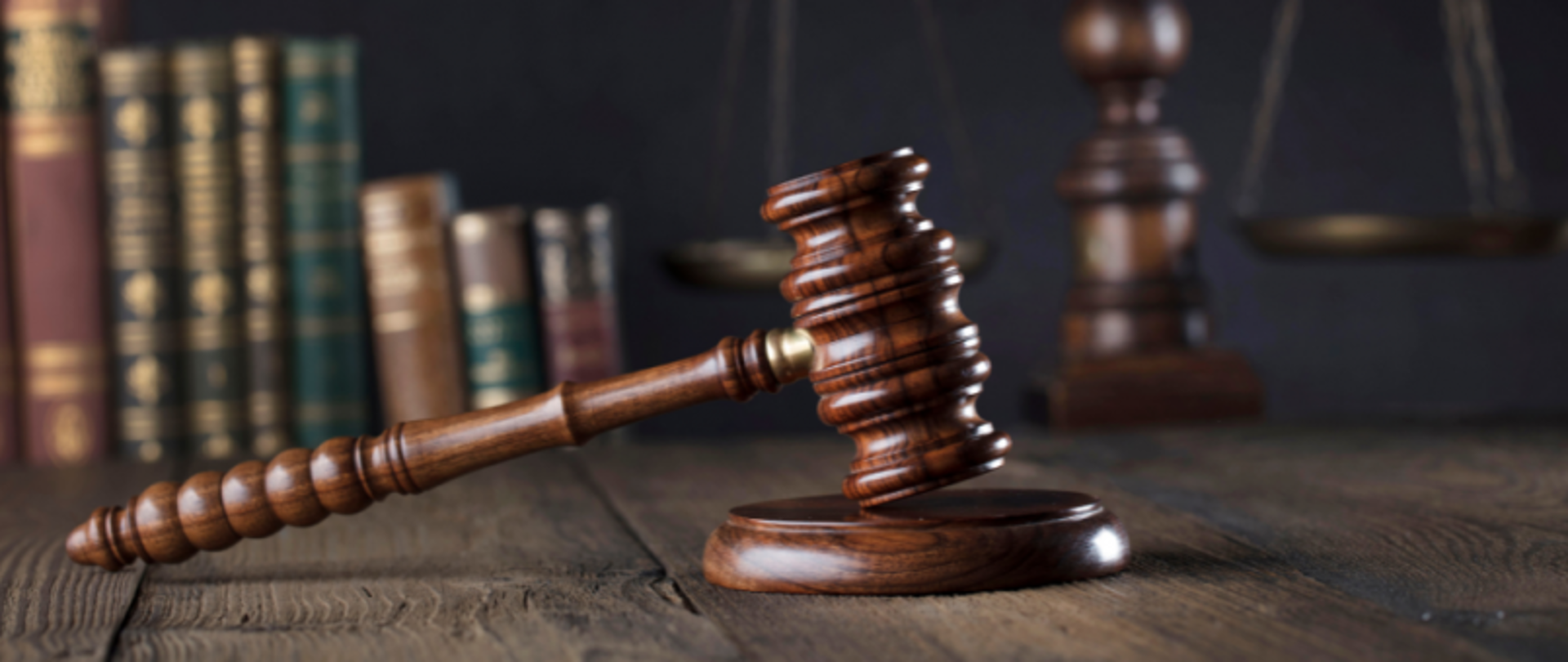 Blat biurka. Na nim młotek sędziowski na podstawce. W tle książki.
