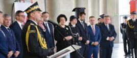 Zastępca komendanta głównego PSP w ubraniu galowym przemawia z za mównicy. W tle zaproszeni goście, 