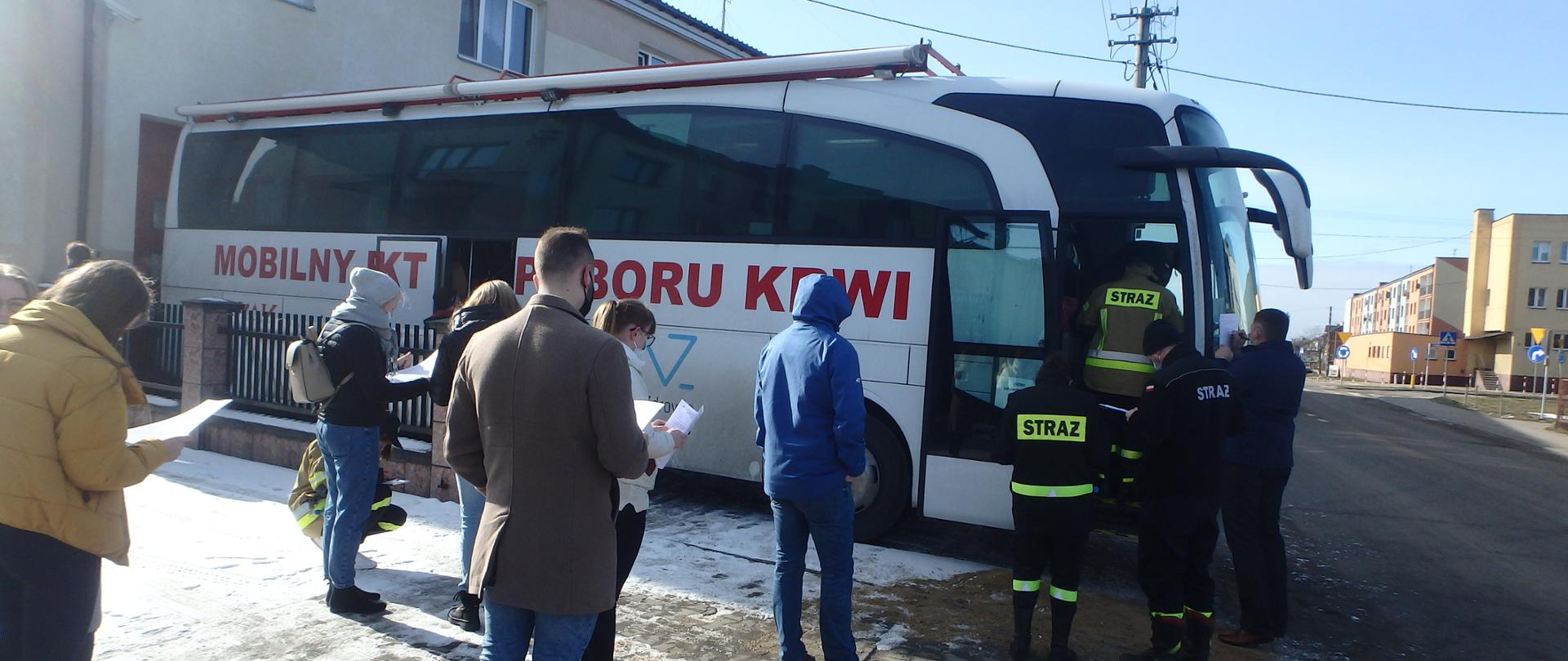 Grupa ludzi czekająca przed autobusem na pobór krwi.